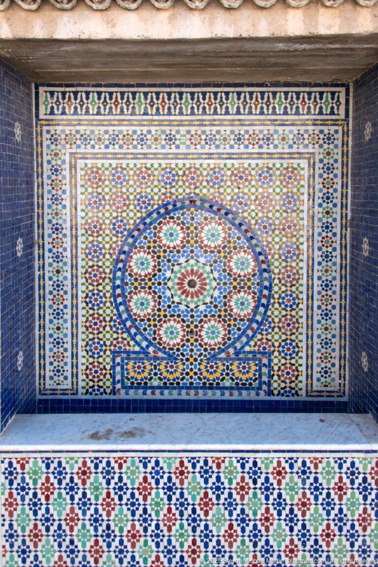 Colorful zellij wall fountain with a circular geometric medallion above a shallow basin.