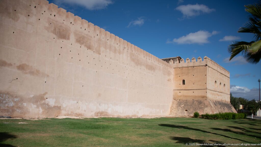 Long crenellated wall meeting a square defensive tower above a green lawn.
