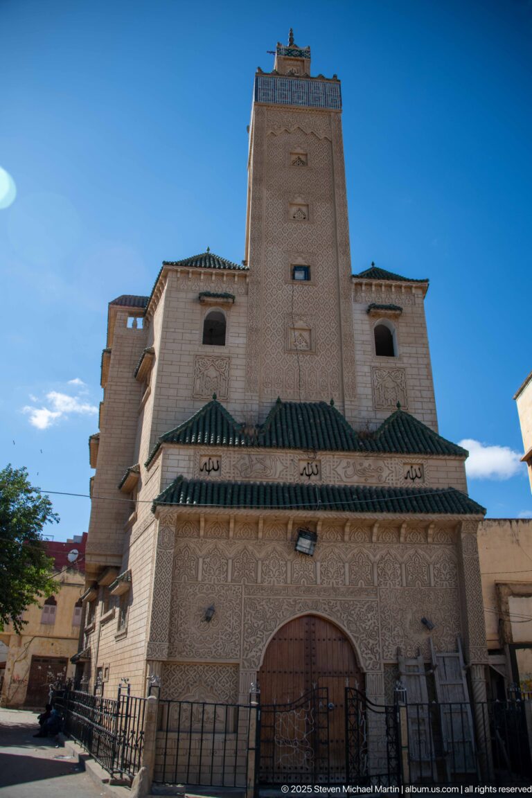 Large symmetrical façade with carved panels, arched wooden entrance, and green-tiled roof sections beneath a tall central block.