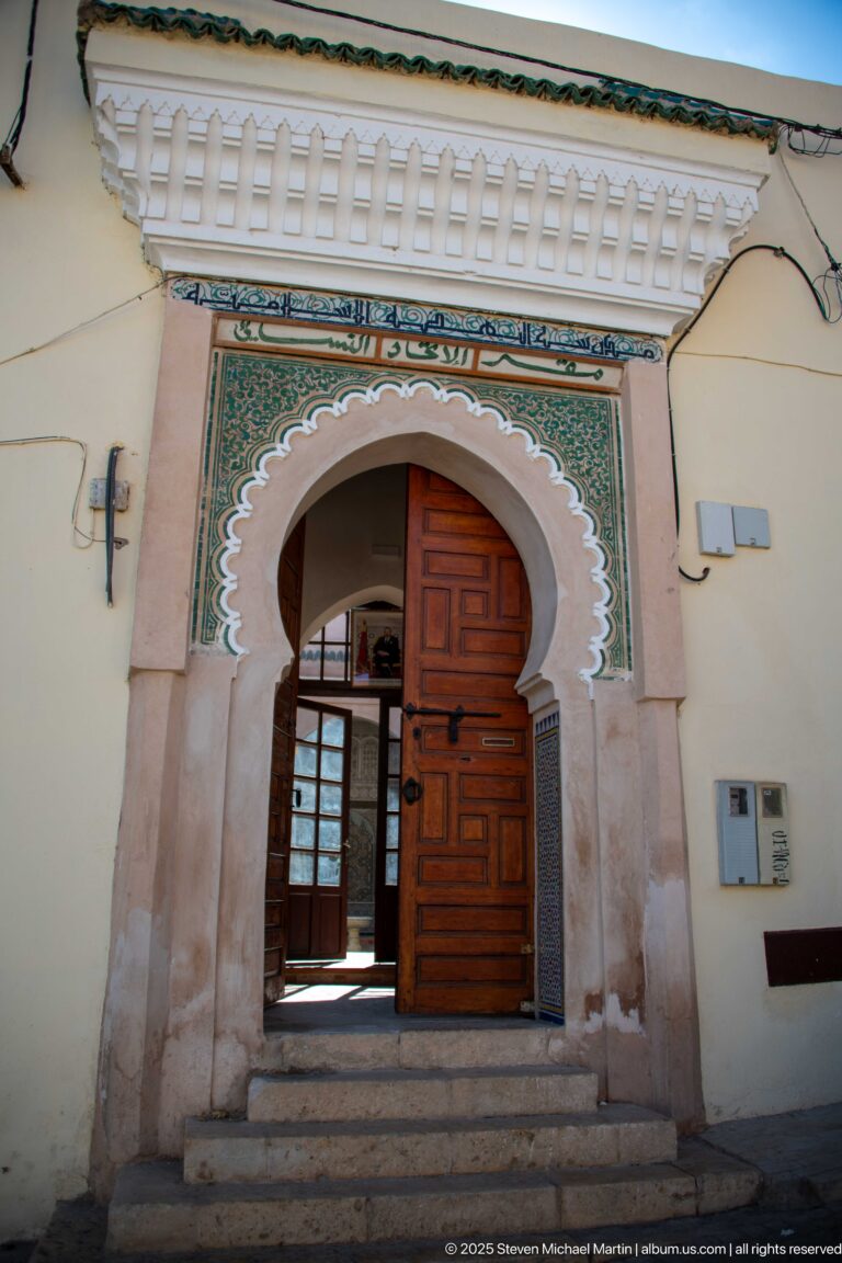 Open wooden doorway within a scalloped decorated arch, reached by shallow stone steps.