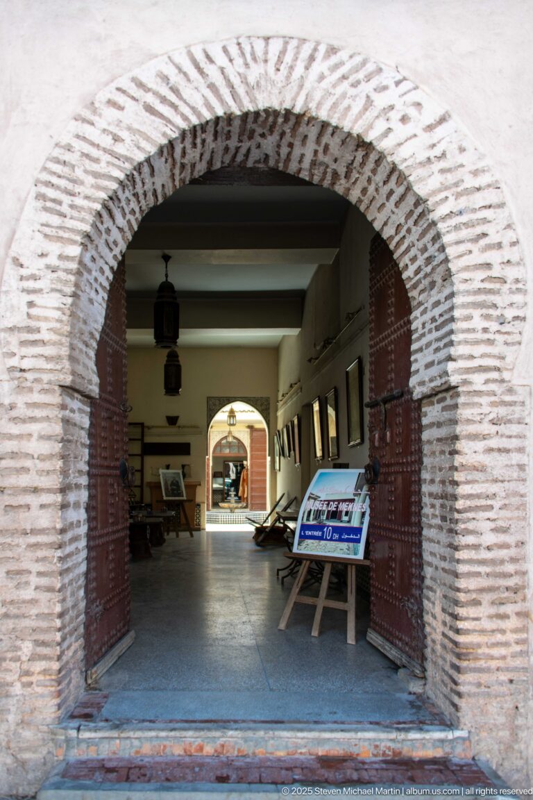 Large brick-edged arch opening into an exhibition interior with display panels and cases.