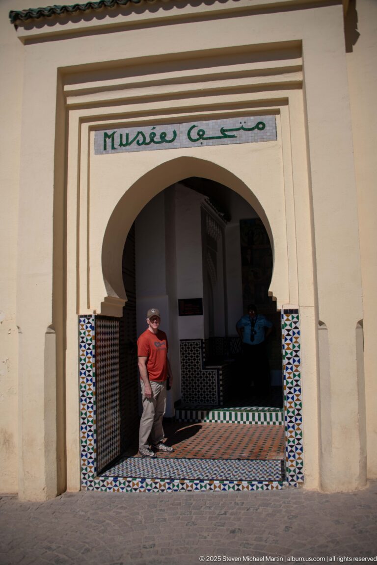 Visitor standing in a horseshoe-arched museum entrance with bilingual signage and zellij around the lower walls.