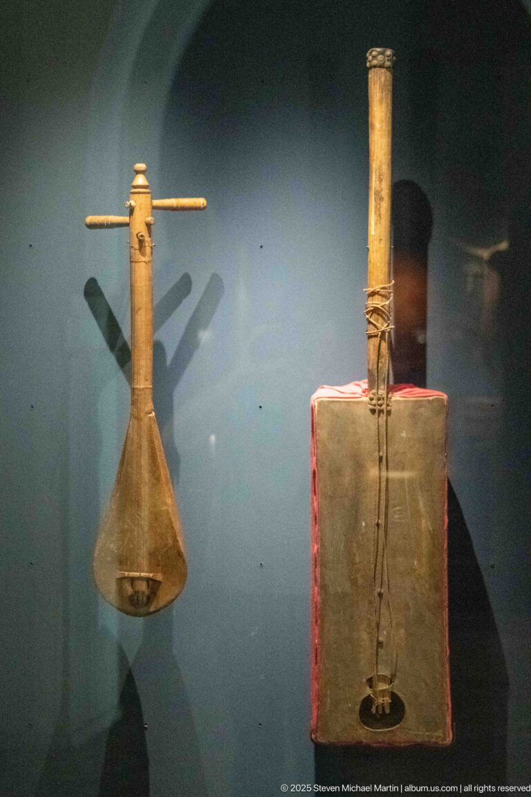 Two traditional string instruments in a museum case, one pear-shaped and one with a rectangular resonator.
