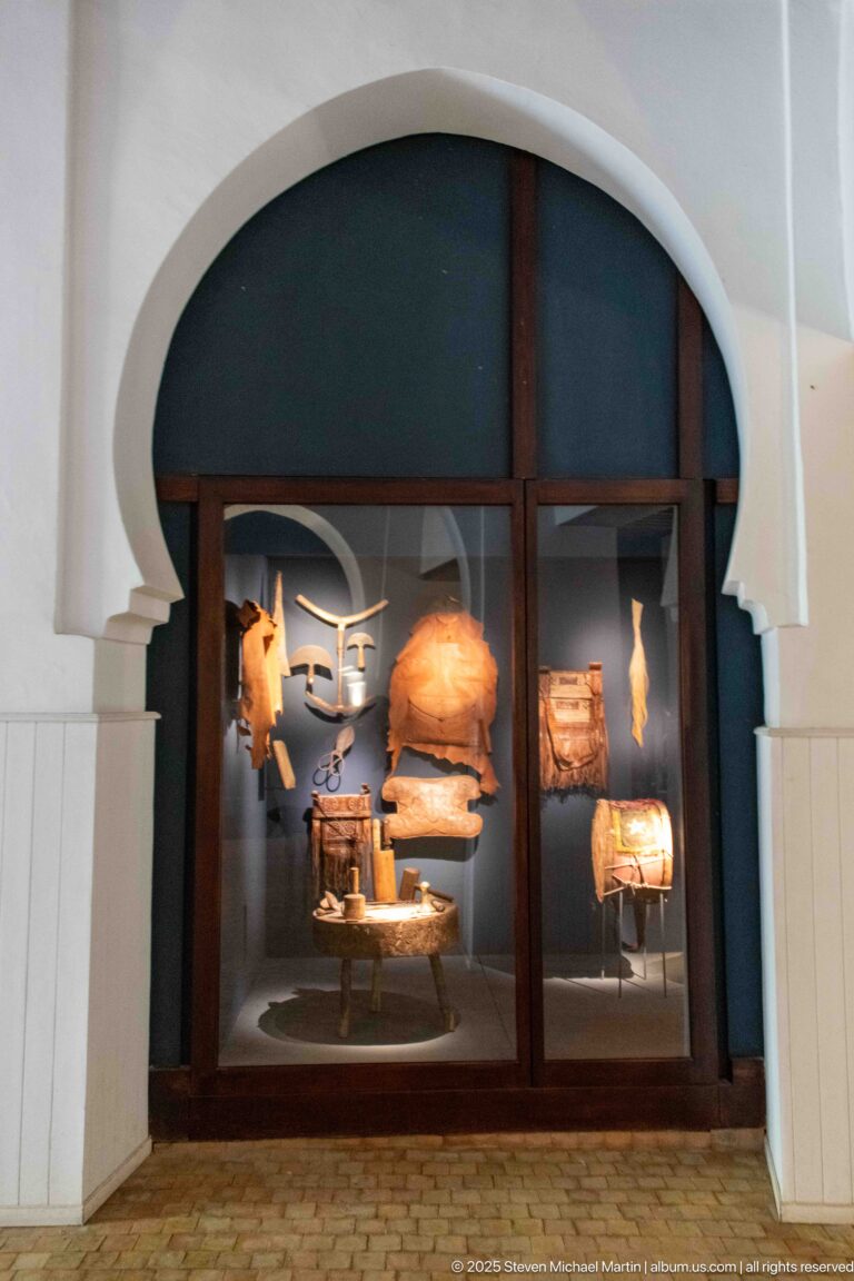 Museum display case containing shaped wooden instrument parts, resonator forms, and small tools.