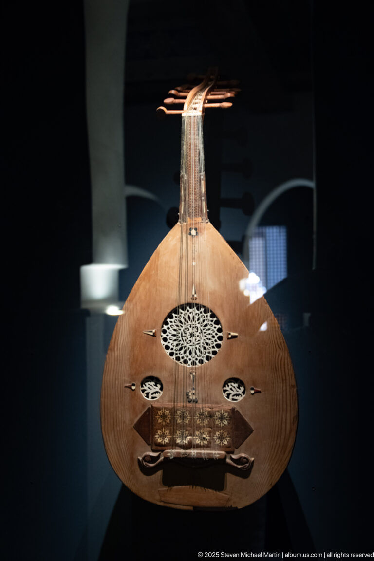 Front view of a wooden oud with pear-shaped body, strings, and ornate circular soundhole rosettes.