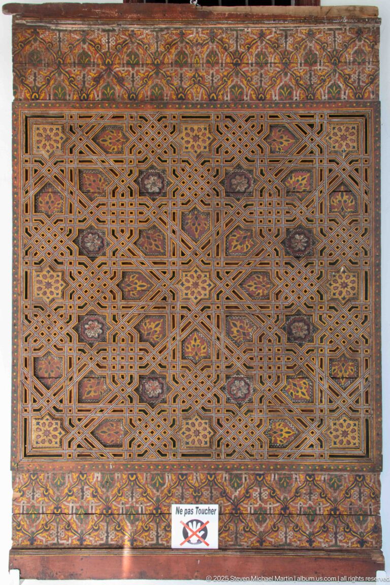 Large carved wooden panel with dense interlaced geometric patterns and a painted floral border.