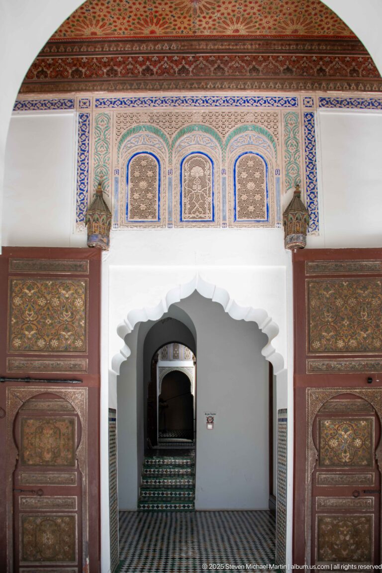 Scalloped interior arch framed by painted wooden panels and decorative bands above a striped tile floor.