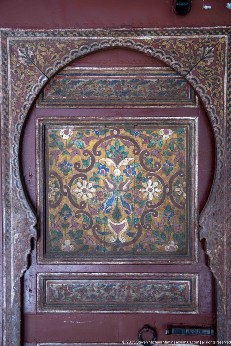 Close-up of a floral painted panel in gold, green, blue, and white within a dark carved wooden surround.