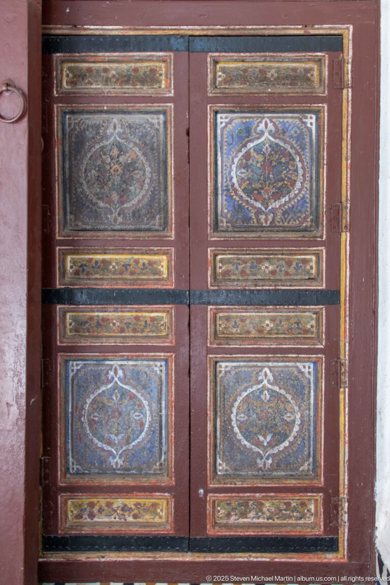 Dark wooden double doors with painted geometric medallion panels and black horizontal braces.