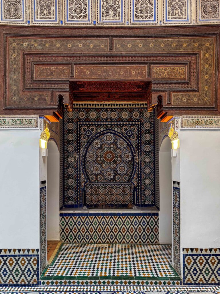 Recessed zellij wall fountain with a circular medallion beneath painted wooden panels and carved brackets.