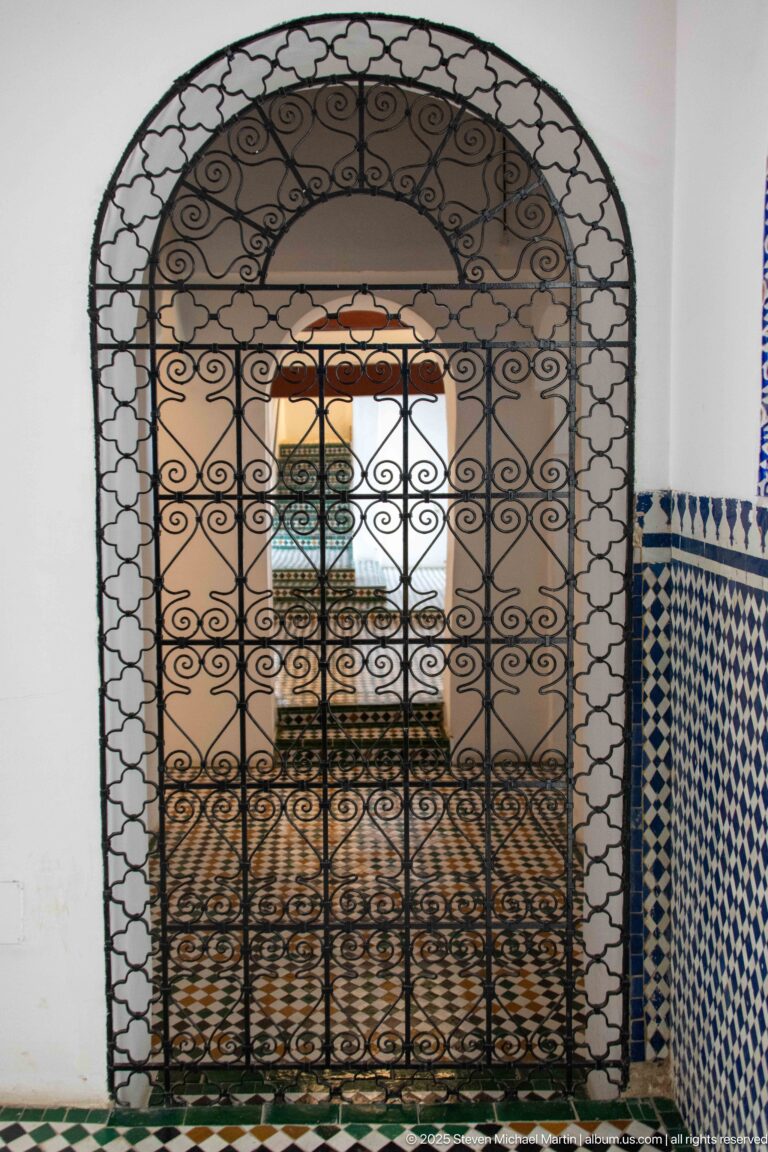Arched wrought-iron grille with dense scrollwork framing a tiled interior beyond.