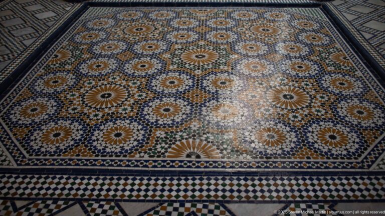 Large multicolored zellij floor filled with radiating rosettes, stars, and geometric border patterns.