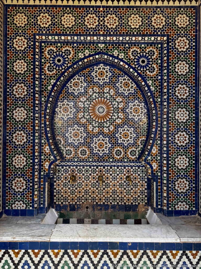 Arched zellij wall fountain with a central radial medallion and low stone basin.