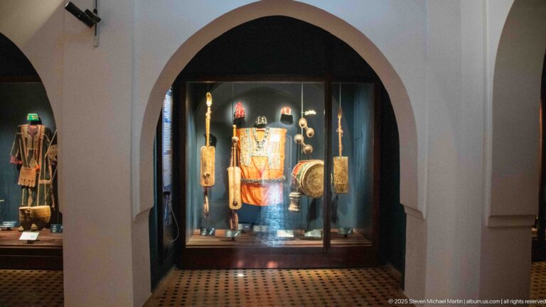 Arched museum doorway framing a glass case with colorful costume, drums, and other traditional objects.