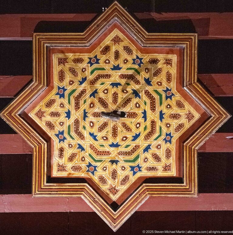 Eight-pointed painted wooden star panel with interlocking gold, green, blue, white, and red geometric patterns.