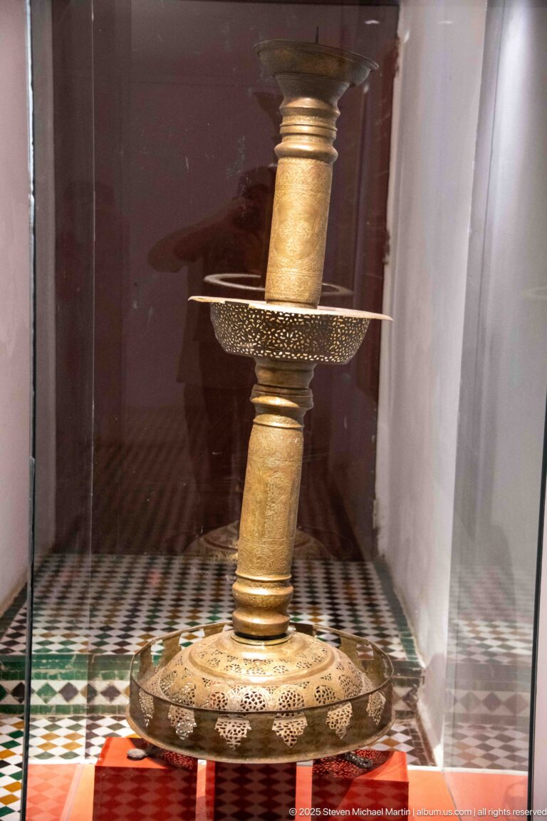 Tall brass- or bronze-colored lampstand with decorated base, pierced tray, and cylindrical shaft.