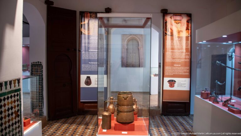 Freestanding museum case with a large metal vessel, flanked by interpretive panels and other displays.
