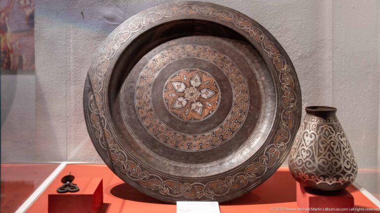 Large engraved circular metal tray with central floral medallion beside a decorated pear-shaped vessel.