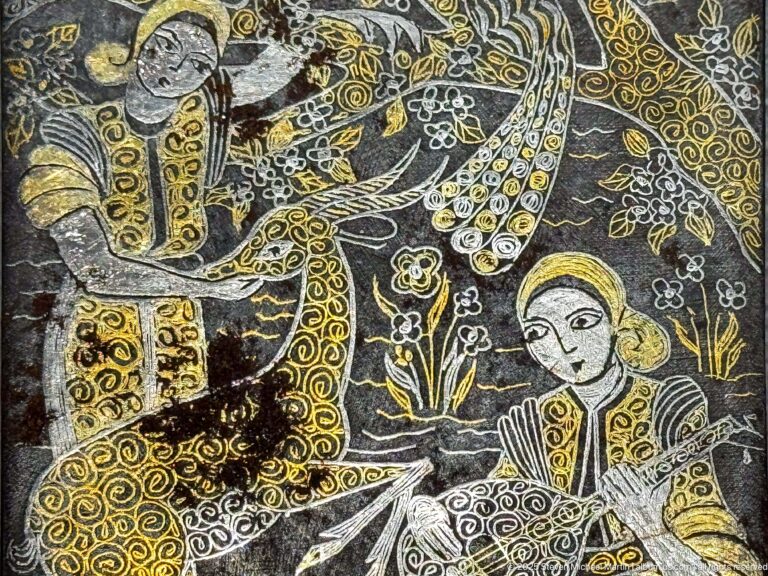 Black embroidered textile with gold and white human figure, birds, foliage, and decorative objects.
