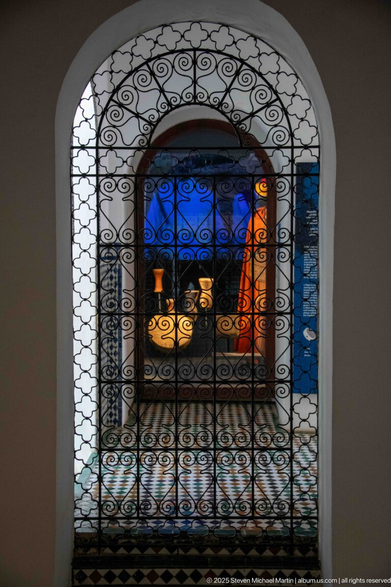 Arched wrought-iron grille silhouetted against blue light with illuminated metal vessels visible beyond.