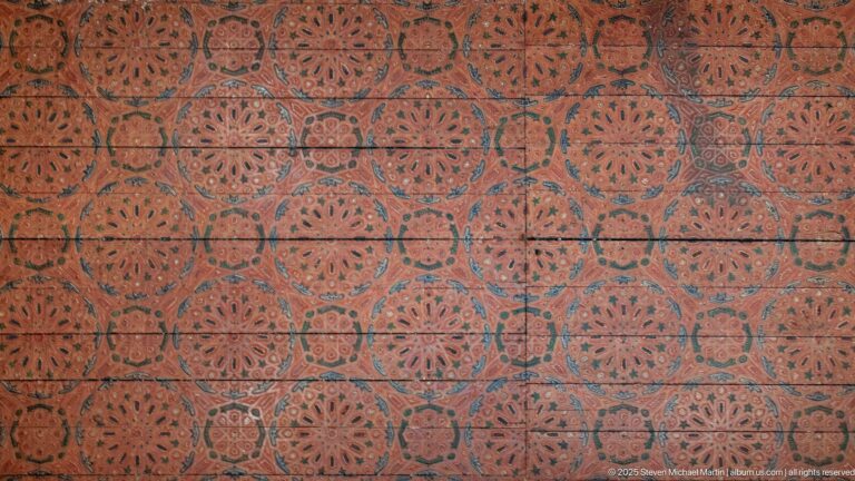Red painted wooden ceiling covered with repeating turquoise and dark floral medallion patterns.