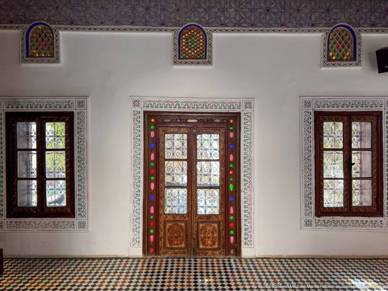 Symmetrical wall with painted double doors, side windows, small stained-glass arches, and black-and-white patterned floor.