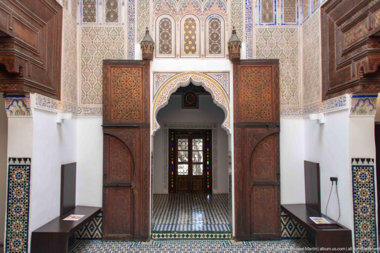 Symmetrical ornate doorway with carved surround, painted wooden side panels, patterned tile, and a glazed door beyond.