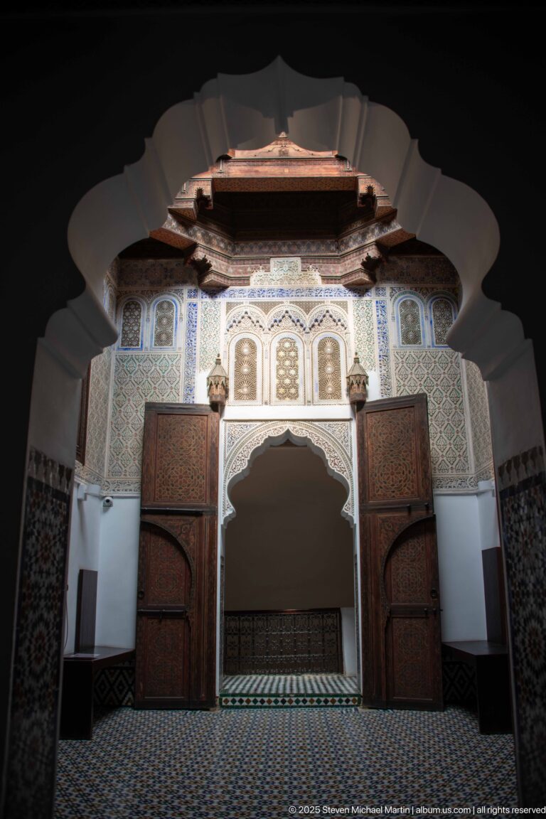 Symmetrical ornate room with open wooden doors, scalloped central arch, carved panels, and patterned tile floor.