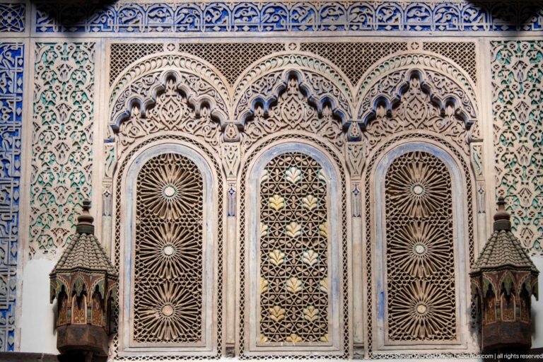Three arched lattice windows with carved rosette screens surrounded by dense blue, green, and white ornament.