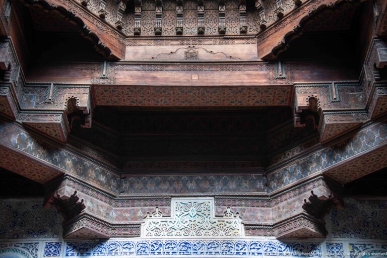Upward view of a deep painted wooden ceiling with carved brackets and multicolored decorative bands.