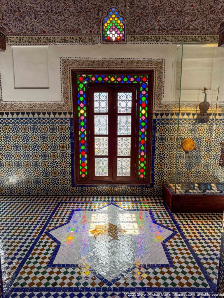 Wooden door with multicolored glass panels casting colored light across a patterned zellij floor.
