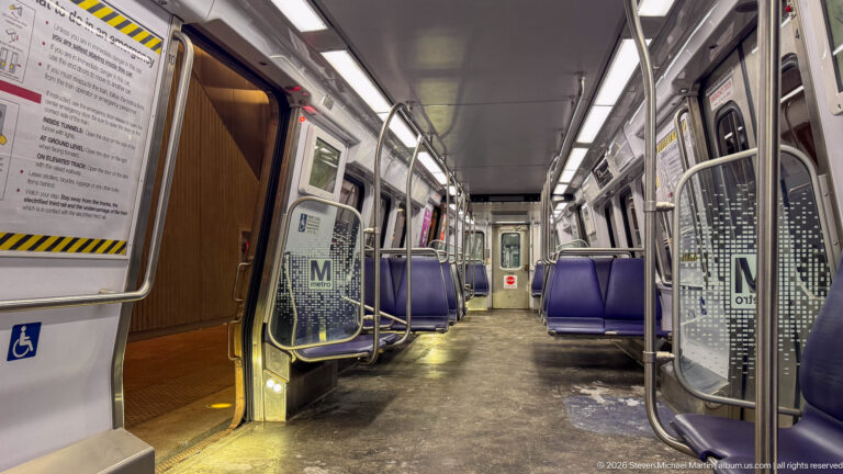 Empty airport people-mover car with purple seats, metal grab rails, route signage, and an accessible doorway.