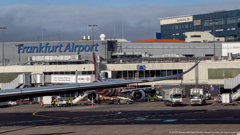 Aircraft at a Frankfurt Airport gate with terminal buildings, jet bridges, service vehicles, and apron equipment.