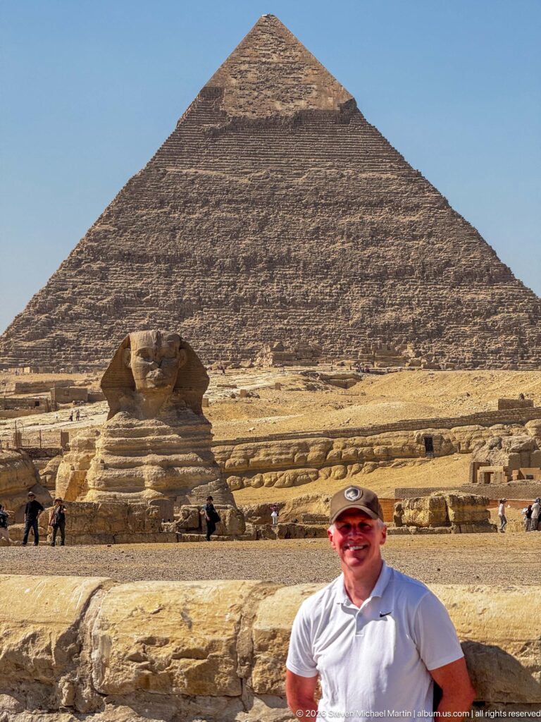 Man in white shirt before the Great Sphinx, with the Pyramid of Khafre filling the background at Giza.