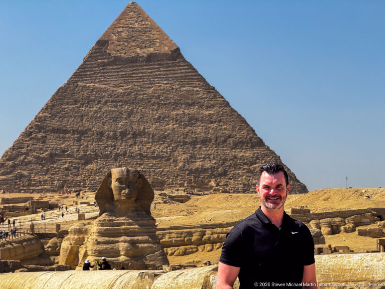 Man in black shirt beside the Great Sphinx, with the Pyramid of Khafre rising behind at Giza.