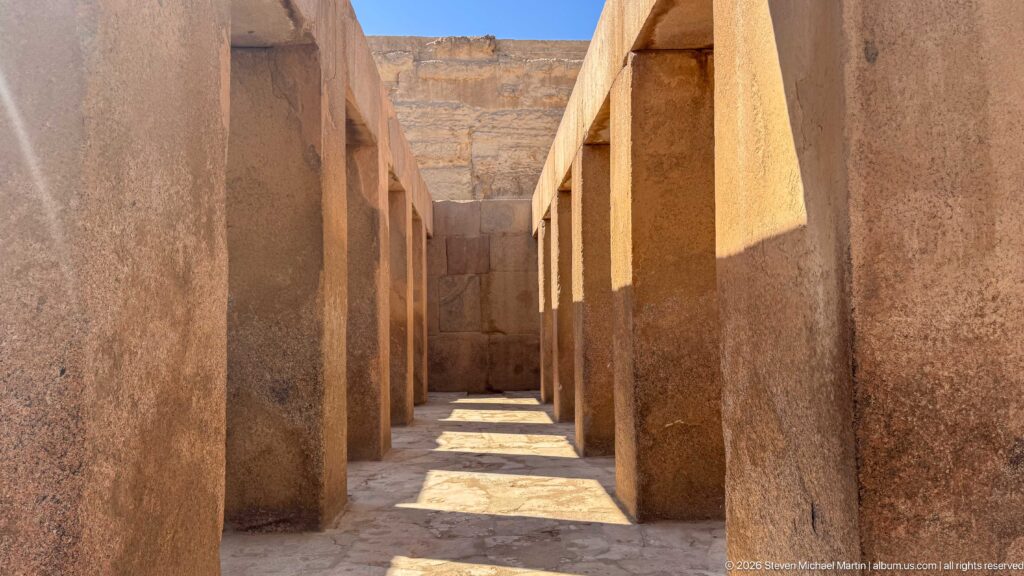 Rows of massive rectangular stone piers forming a sunlit interior passage at an ancient Egyptian temple in Giza.