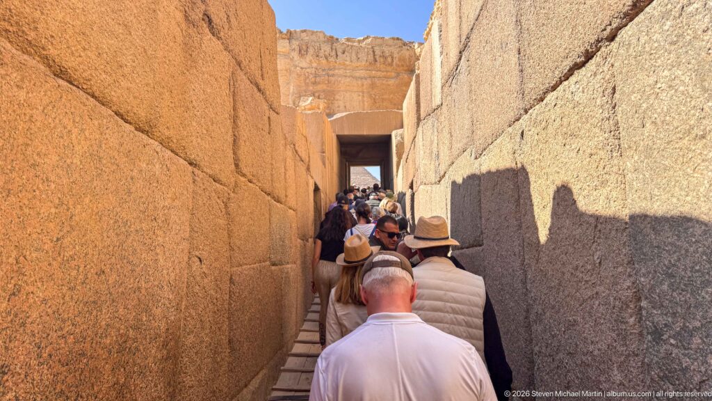 Visitors walking through a narrow corridor between massive fitted stone walls at the Giza pyramid complex.