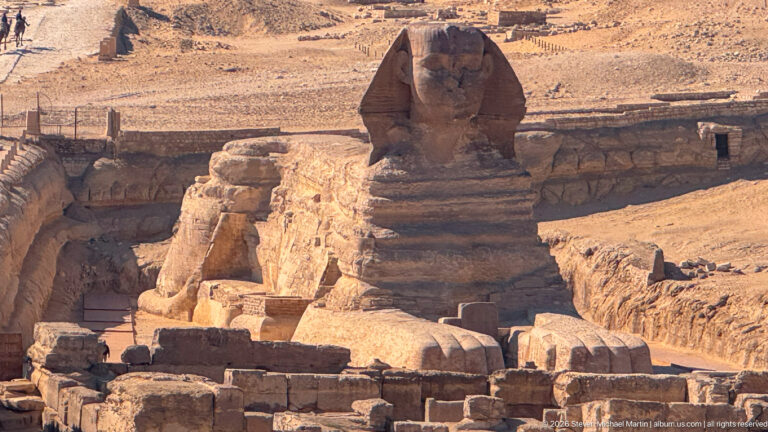 Elevated rear three-quarter view of the Great Sphinx showing its back, head, and excavated limestone enclosure.