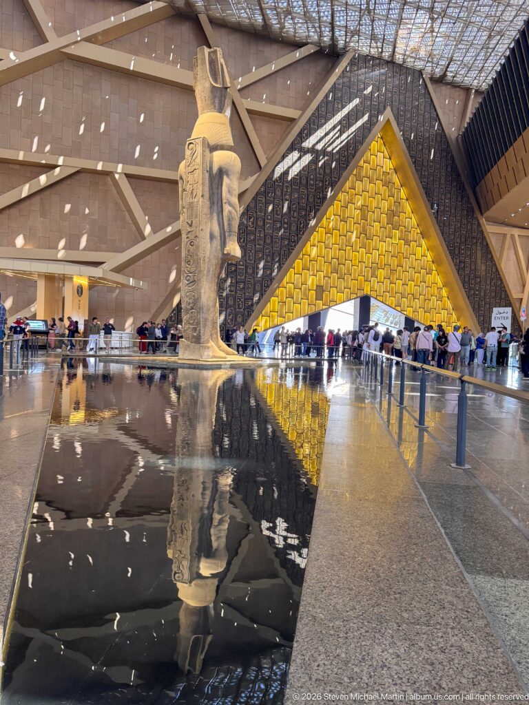 Colossal granite statue of Ramesses II aligned with the Grand Hall reflecting pool and luminous triangular wall.