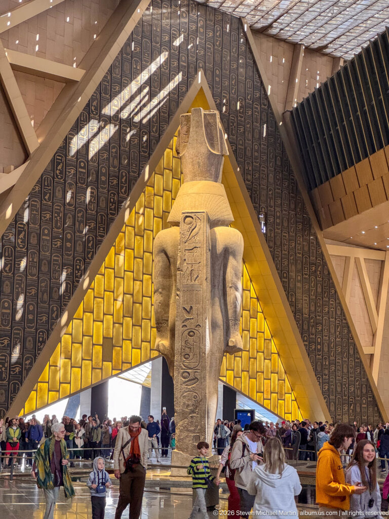 Rear view of the colossal granite statue of Ramesses II in the Grand Hall, its back pillar facing a bright triangular wall.
