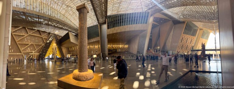 Tall red-granite Column of King Merenptah rising from its base inside the Grand Egyptian Museum's Grand Hall.