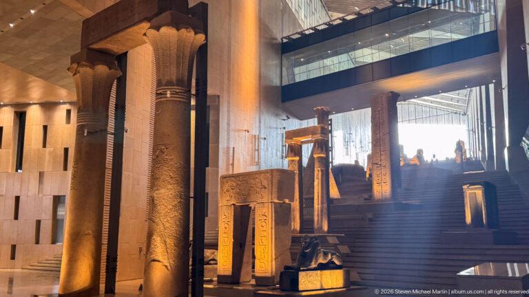 Tall ancient Egyptian columns and doorway fragments covered with hieroglyphs beside the ascending Grand Staircase.