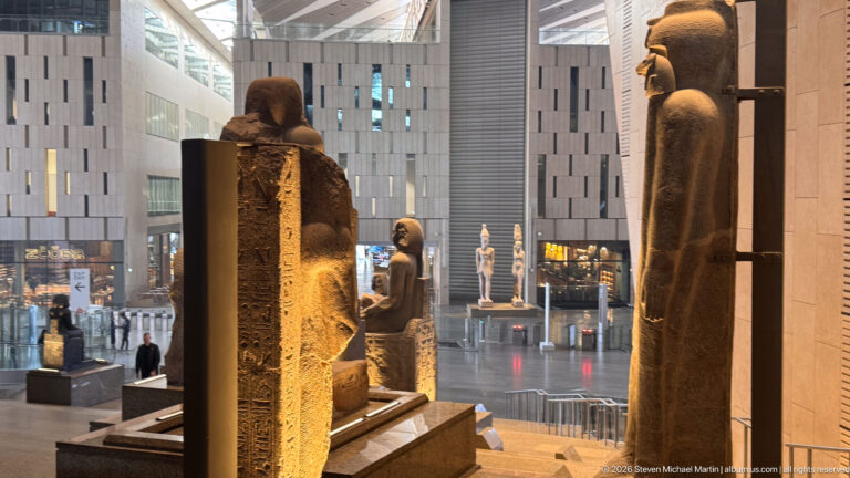 Rear and side views of ancient Egyptian statues on the staircase, including a tall back pillar carved with hieroglyphs.