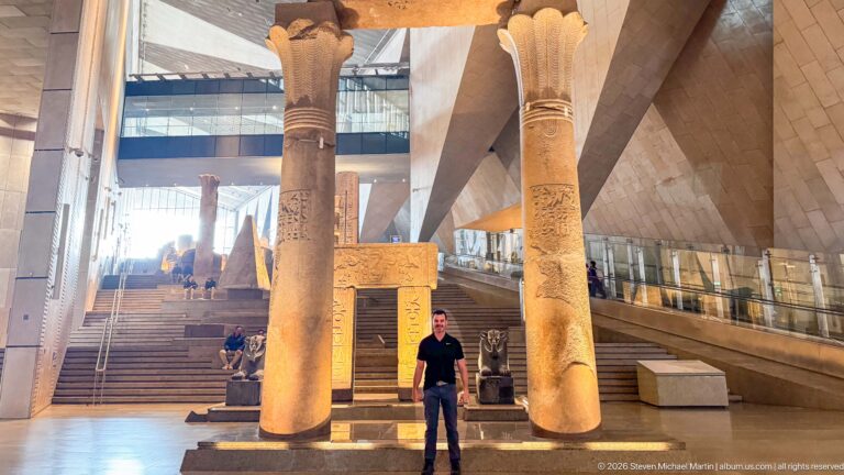 Man standing between two enormous papyrus-form columns with carved shafts at the base of the Grand Staircase.