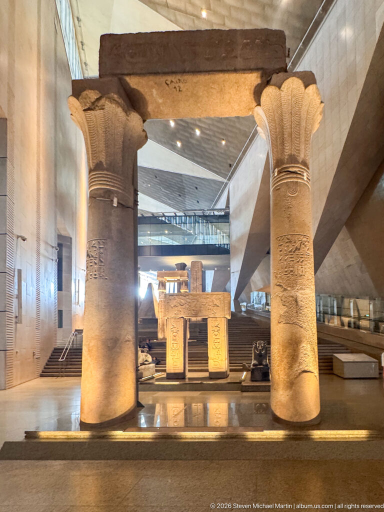 Centered view through two huge papyrus-form columns toward a smaller inscribed stone gateway and staircase beyond.