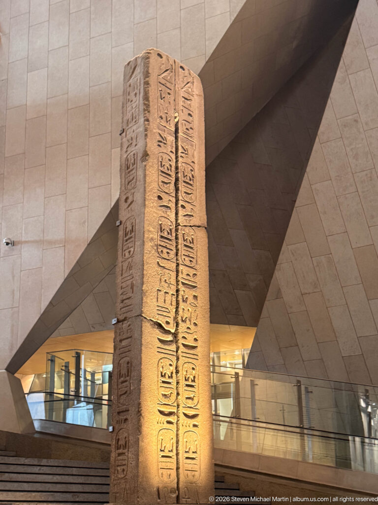Close view of a tall stone pillar carved with vertical hieroglyphic inscriptions beside the museum staircase.
