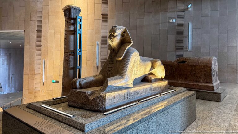 Recumbent stone sphinx with human head, lion body, extended forepaws, and an inscribed base.