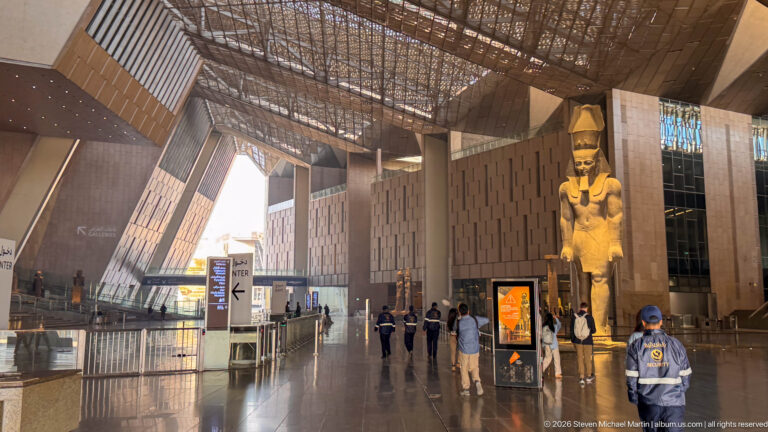 Colossal standing statue of Ramesses II in the Grand Hall, towering above visitors beneath the high patterned roof.