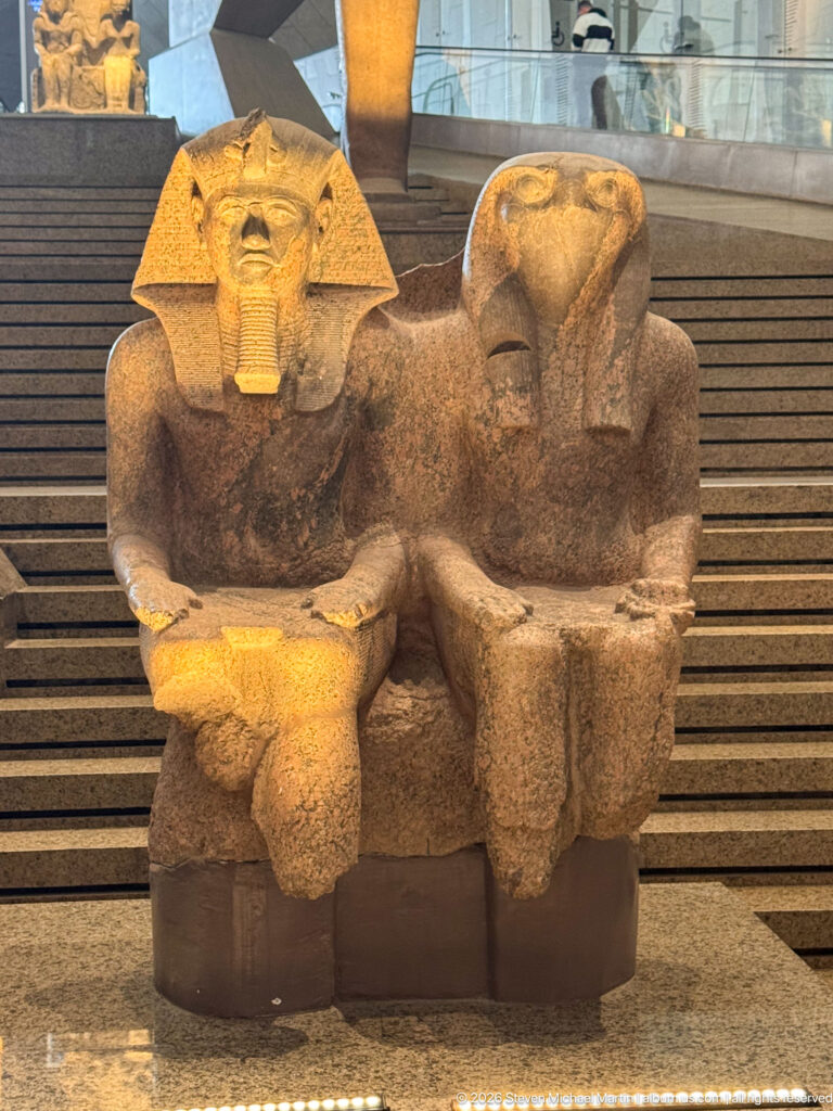 Fragmentary joined stone group of two seated figures, one retaining a broad royal headdress and face.