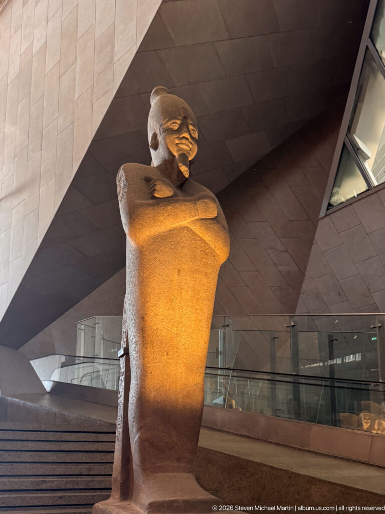 Low-angle view of a large fragmentary standing male stone statue with arms held across the torso.
